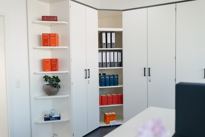 Moderne Büroeinrichtung mit weißen Regalen und Ordnern in Blau und Orange.