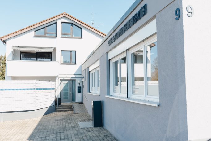 Helles Gebäude mit drei Fenstern und einem Eingangsbereich, Hausnummer 9.