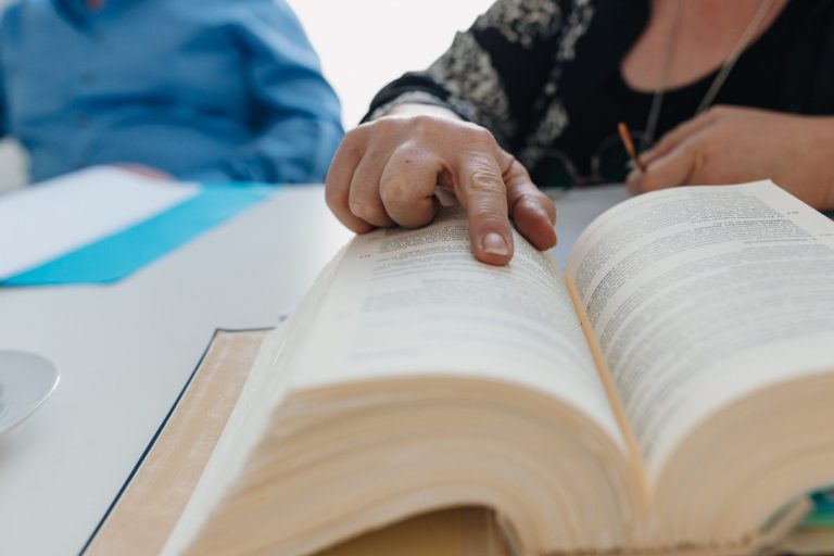 Verfahrensrecht Eine Hand zeigt auf eine geöffnete Gesetzbuch auf einem Tisch, um Verfahrensrecht sinnbildlich dazustellen.