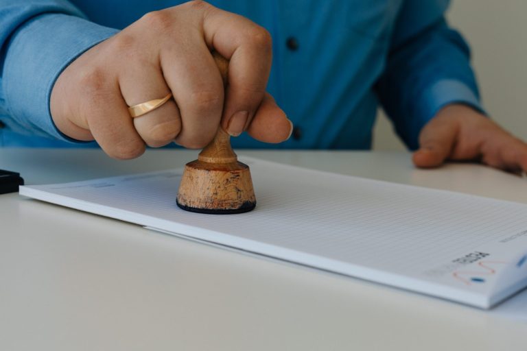 Testamentsvollstreckung Eine Hand stempelt ein Dokument auf einem Tisch, um die Testamentsvollstreckung darzustellen.